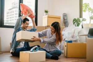 Asian young couple carrying big cardboard box for moving in new